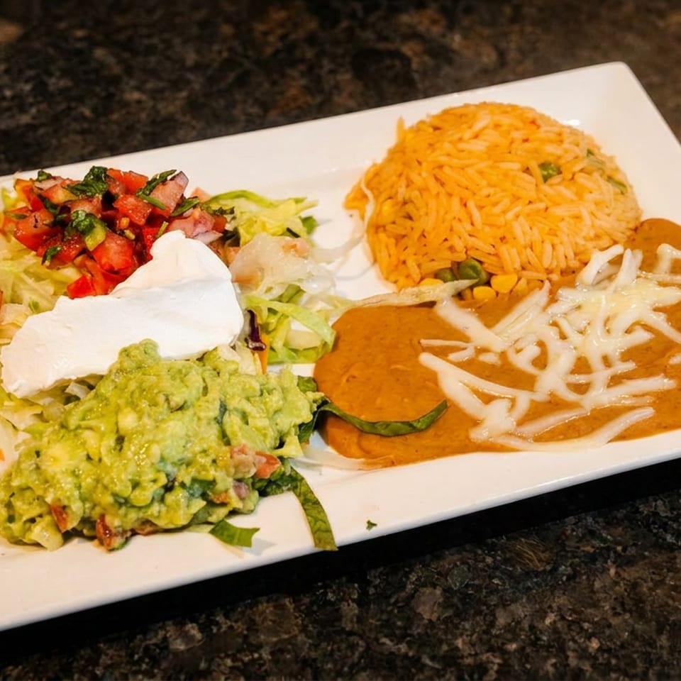 A white rectangular plate holds Mexican rice, refried beans, guacamole, pico de gallo, and sour cream.