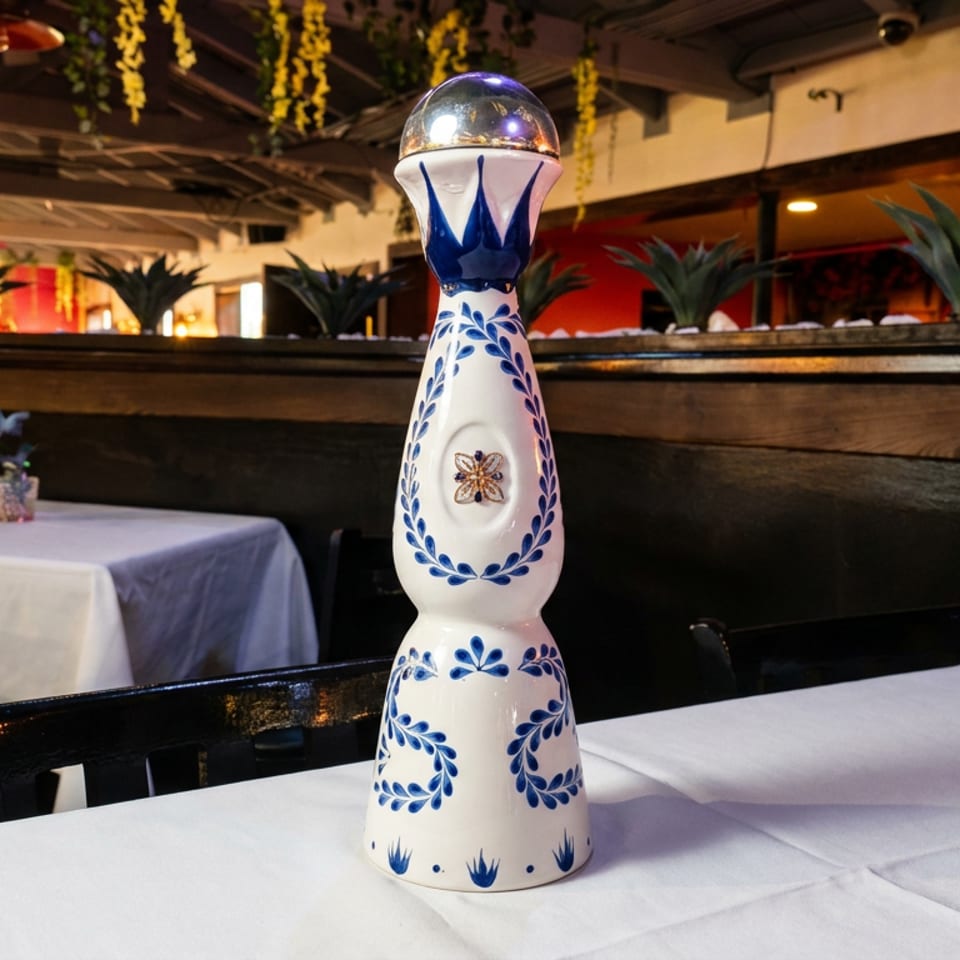 A decorative blue and white bottle on a white tablecloth in a restaurant with dark wood and plants.