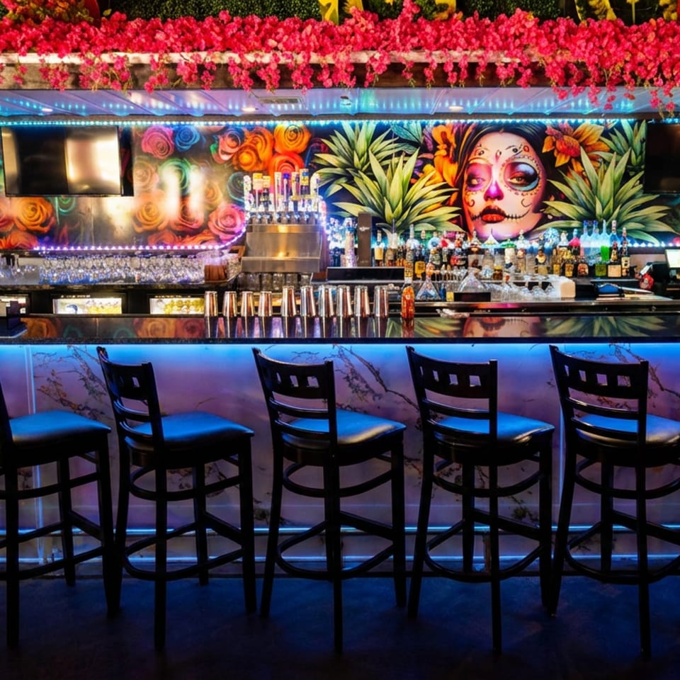A vibrant bar with blue under-lighting, bar stools, and a colorful mural featuring a Day of the Dead skull.
